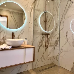 Salle de bain moderne en marbre et équipée avec un miroir en rond.