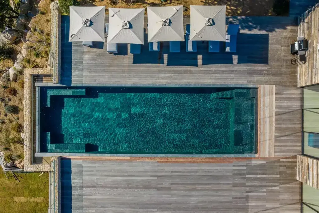 Vue aérienne de la piscine chauffée et sa grande terrasse en bois, équipée de transats et parasols.