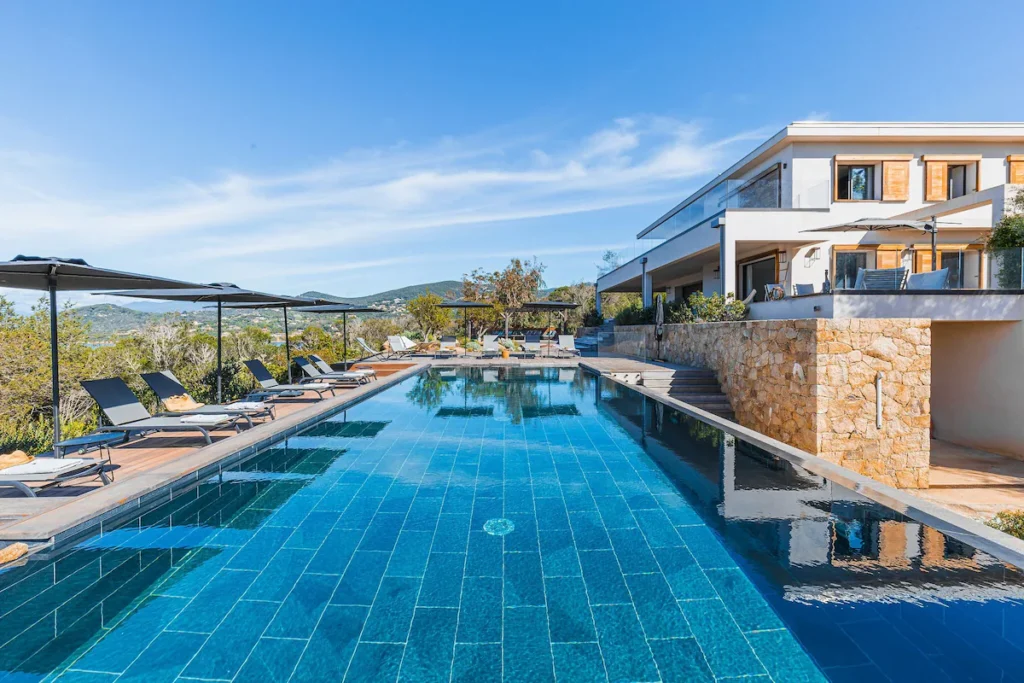 Vue sur toute la piscine et sa grande terrasse équipé de transat et parasol.